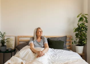 A calm woman sitting in bed practicing mindfulness and looking to her left as she focuses on how to be more present in her daily life.