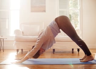 Woman practices Downward-Facing Dog Pose in her house