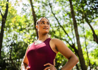 A woman with her hands on her hips, doing an outdoor workout in a park. She is feeling strong and confident.