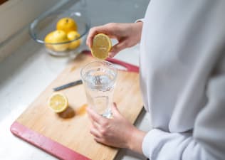 A person squeezing lemon into a glass of water to help them stay hydrated.