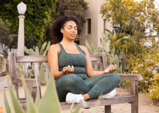 Woman meditating outside on a park bench in workout clothes