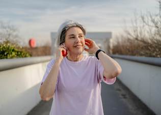 A woman walking outside and listening to music on a warm day. She is exercising to help ease arthritis symptoms.