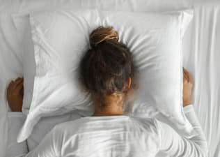 A woman who can't fall asleep puts her head down into her pillow with her fists next to her pillow.