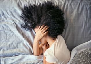 A woman lying in bed on her side as she has morning anxiety. Her hand is covering her face.