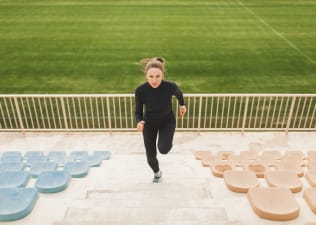 A woman running up a flight of stairs at an outdoor stadium.