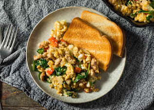 A healthy breakfast option of scrambled eggs with veggies mixed in and some whole-wheat toast on the side.