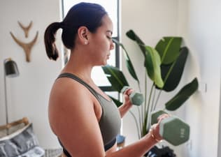 A young woman lifting dumbbells at home.