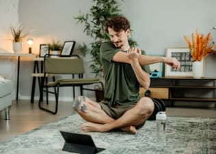 A man stretching his arms while doing a guided stretching class on his tablet after a workout.