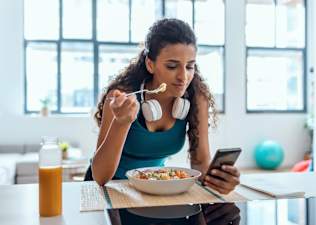 A woman eating after a workout and looking at her phone.