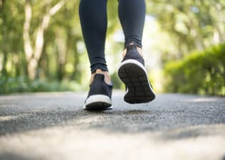 A close-up photo of a person walking outside while wearing black walking shoes and leggings. Learn how to treat and prevent blisters in this article.