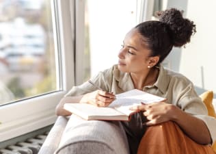 A young woman sitting on her couch and practicing a gratitude exercise by writing in her gratitude journal.