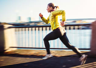 A woman practicing lactate threshold training by sprinting. She's running outside on a path near a river.