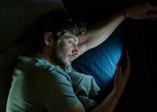 A man lying in bed and staring at his phone at night.