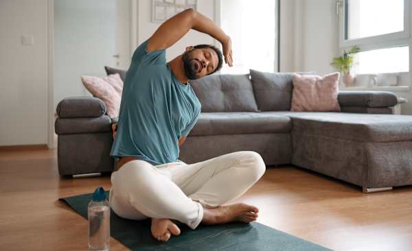 A man taking a rest day from exercise and doing some gentle stretches at home on a workout mat.
