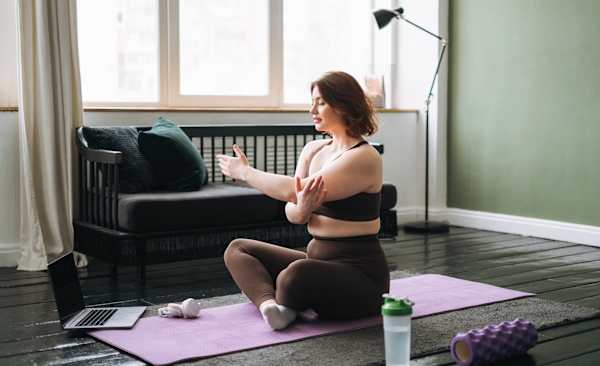 A woman sitting down on a yoga mat, stretching her arms on a rest day.