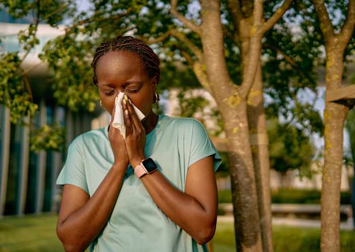 A woman blowing her nose into a tissue during an outdoor workout. She's exercising with allergies.