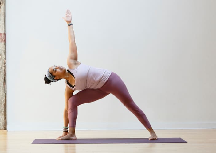 A woman practicing yoga for longevity. She is in Triangle Pose on a mat in a large room.