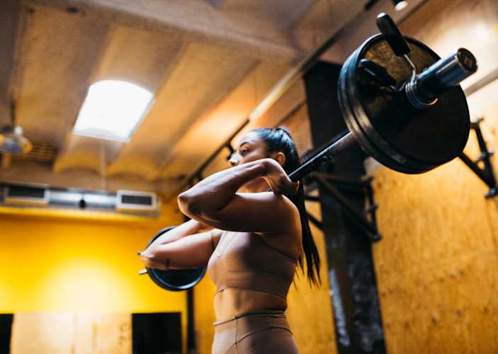 Woman lifting a loaded barbell in a gym doing a strength training program for increasing training volume.
