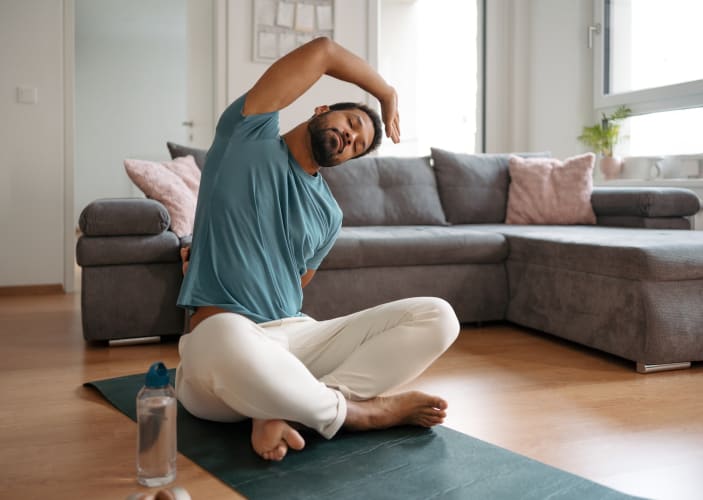 A man taking a rest day from exercise and doing some gentle stretches at home on a workout mat.