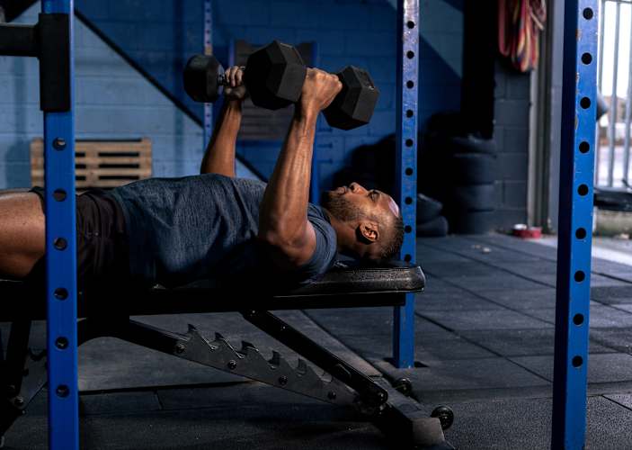 Man in the gym making the mistake of ego lifting by bench pressing dumbbells that are too heavy for him.