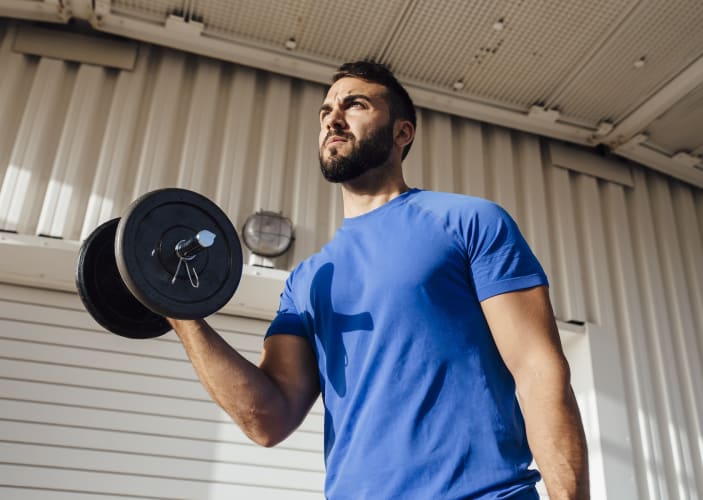 A man lifting a dumbbell while standing near a wall. Learn if working out increases testosterone in this article.