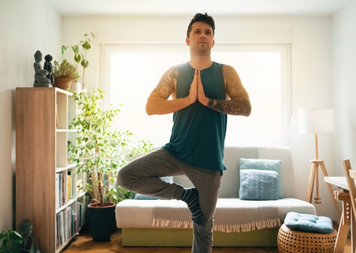 Man doing Tree Pose (yoga posture) inside 