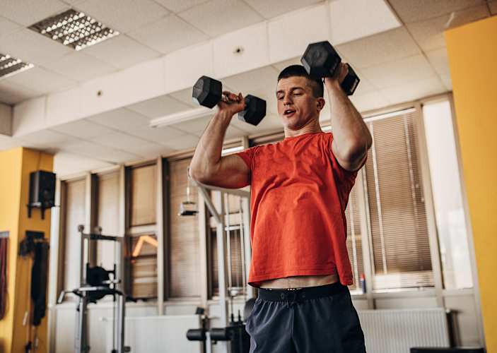 Man doing the thrusters exercise with dumbbells in a gym.