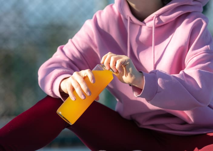 A woman drinking an orange electrolyte drink before or after a workout.