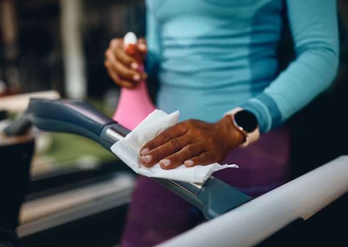 A close-up photo of a woman practicing proper gym etiquette by wiping down a cardio machine she just used.