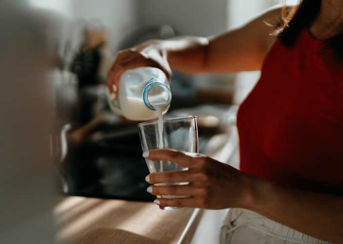 Close-up photo of a woman pouring a glass of milk in her kitchen. She's drinking milk to help build muscle. 