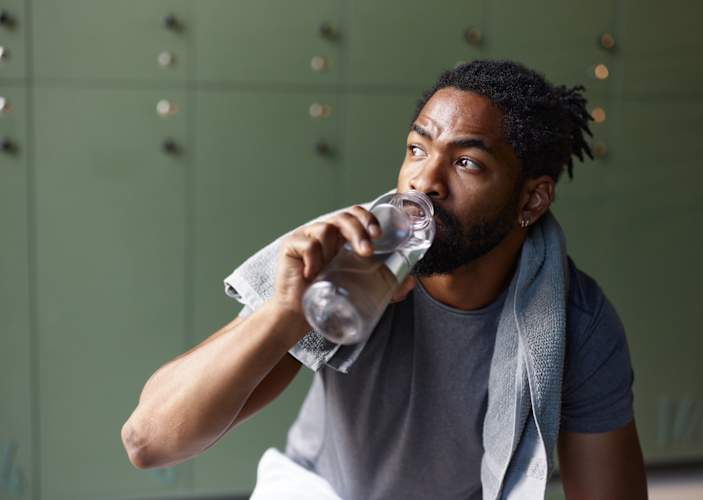 A man drinking water in a gym locker room. He is drinking water to gain muscle.
