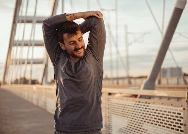 A man smiling and stretching his arms before going on an outdoor run in the morning.