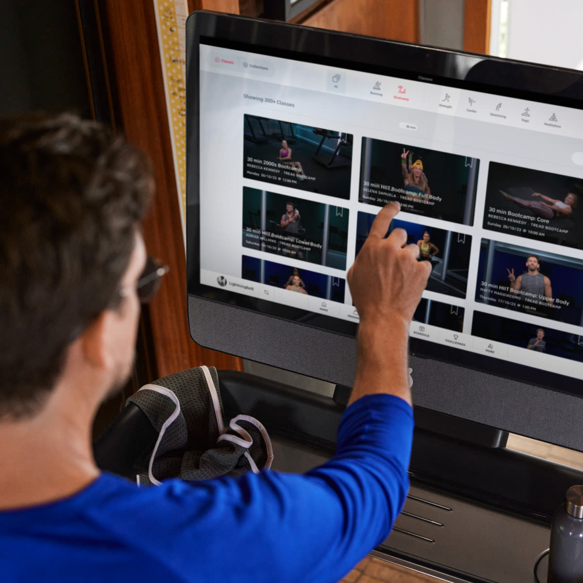 A man running on the Peloton Tread touching the screen. 