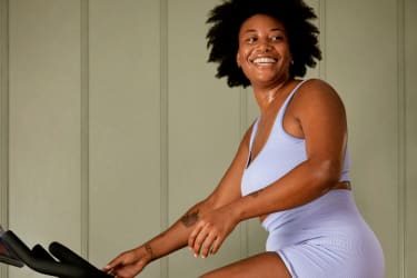 A Lady smiling whilst sitting on a Peloton Bike