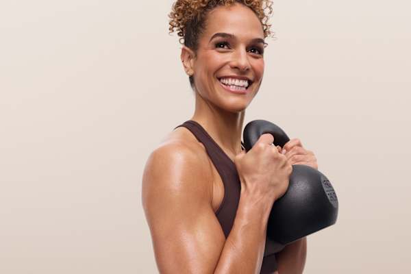 Smiling instructor holding a kettlebell close to her chest during a strength training workout.