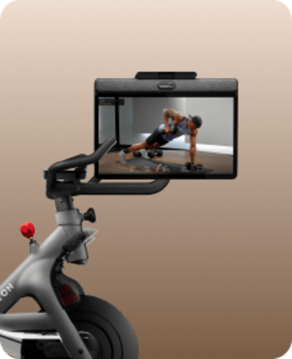 Close-up of a Peloton Bike's handlebars and swivel screen showing a strength training workout with an instructor.