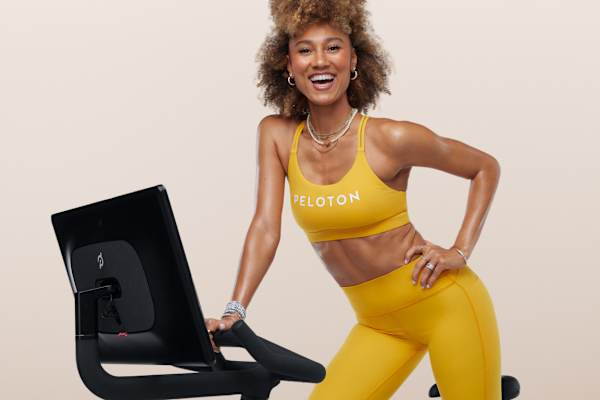 Smiling instructor leaning on the handlebars of a Peloton Bike during a cycling session.