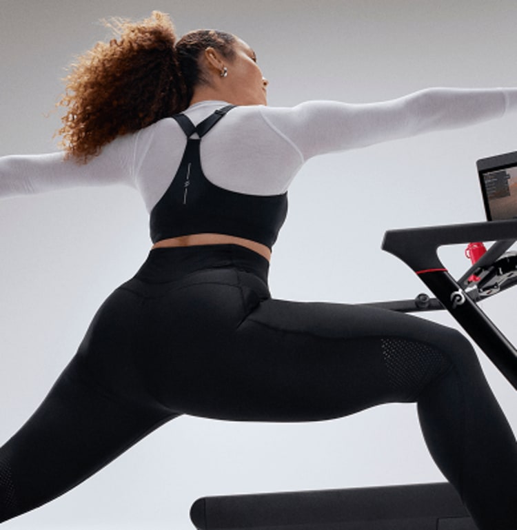 A lady performs stretch beside a Peloton tread whilst following a Peloton class on the Peloton tread swivel screen