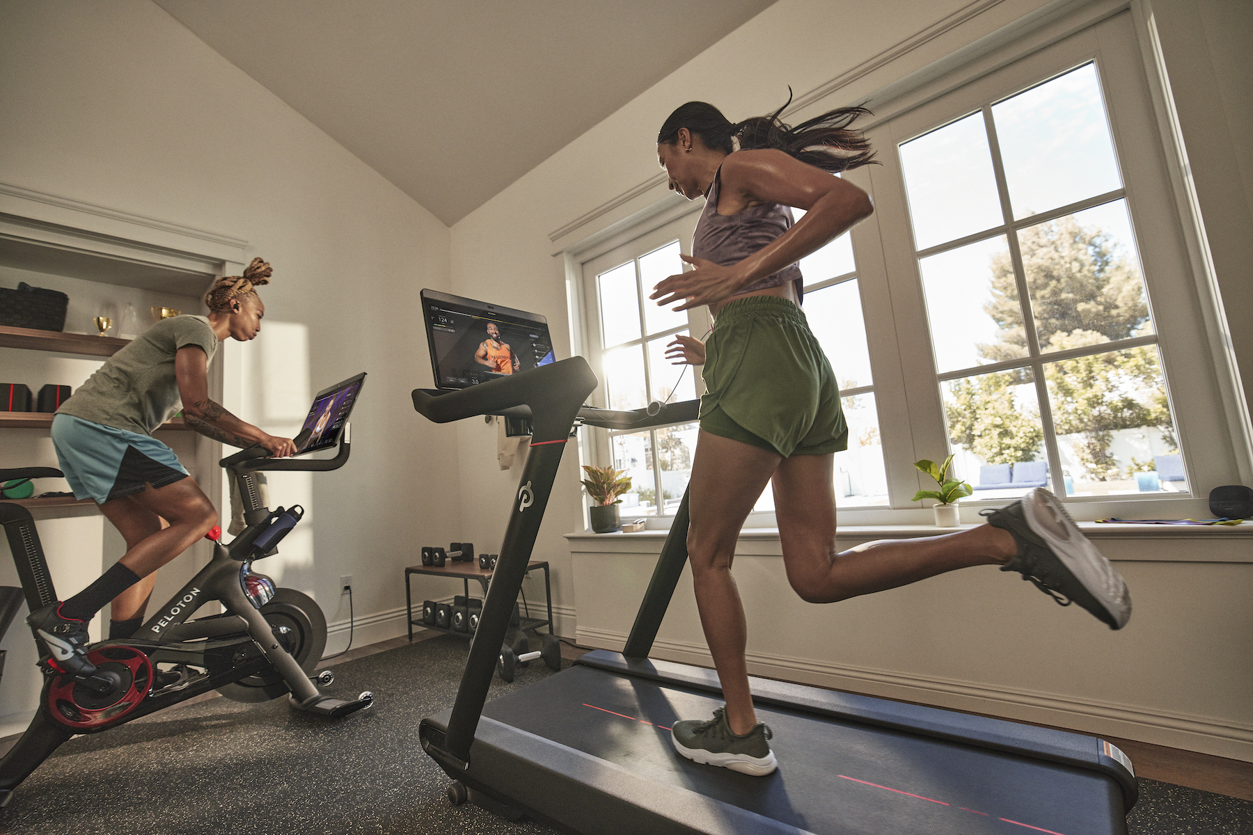 One person runs on the Peloton Tread at home and another cycles on a Peloton Bike