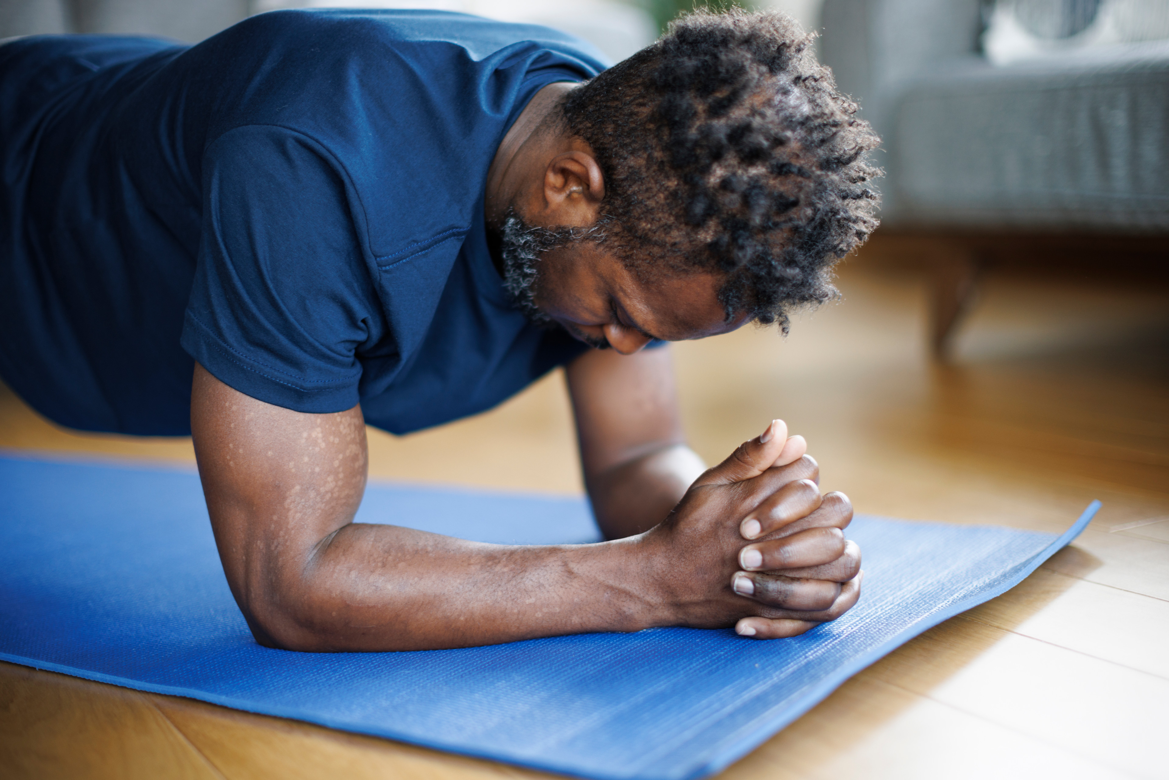 Man in a blue shirt doing a forearm plank during a bodyweight workout at home