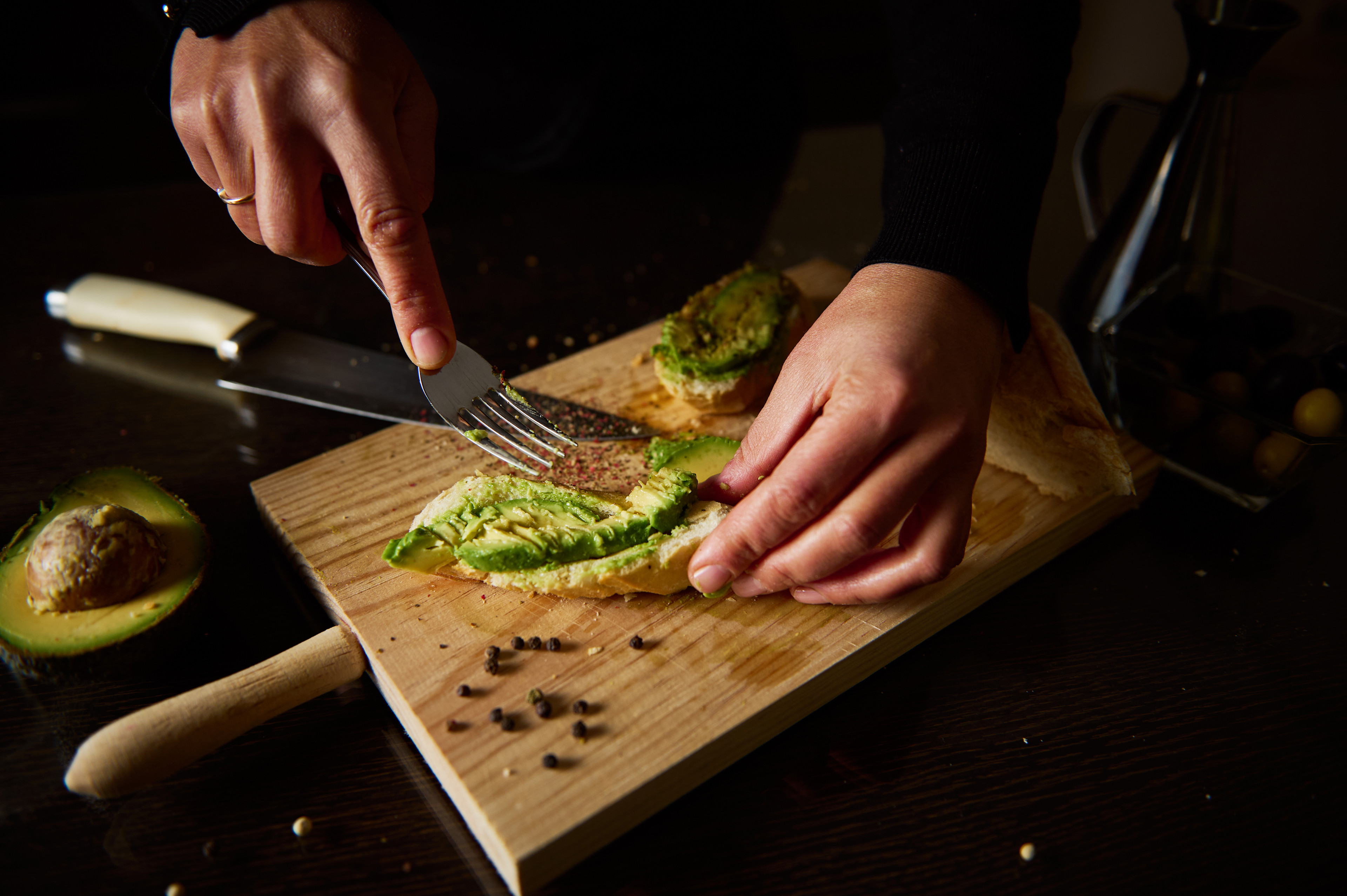 A close-up photo of a person preparing avocado toast as a healthy late-night snack.