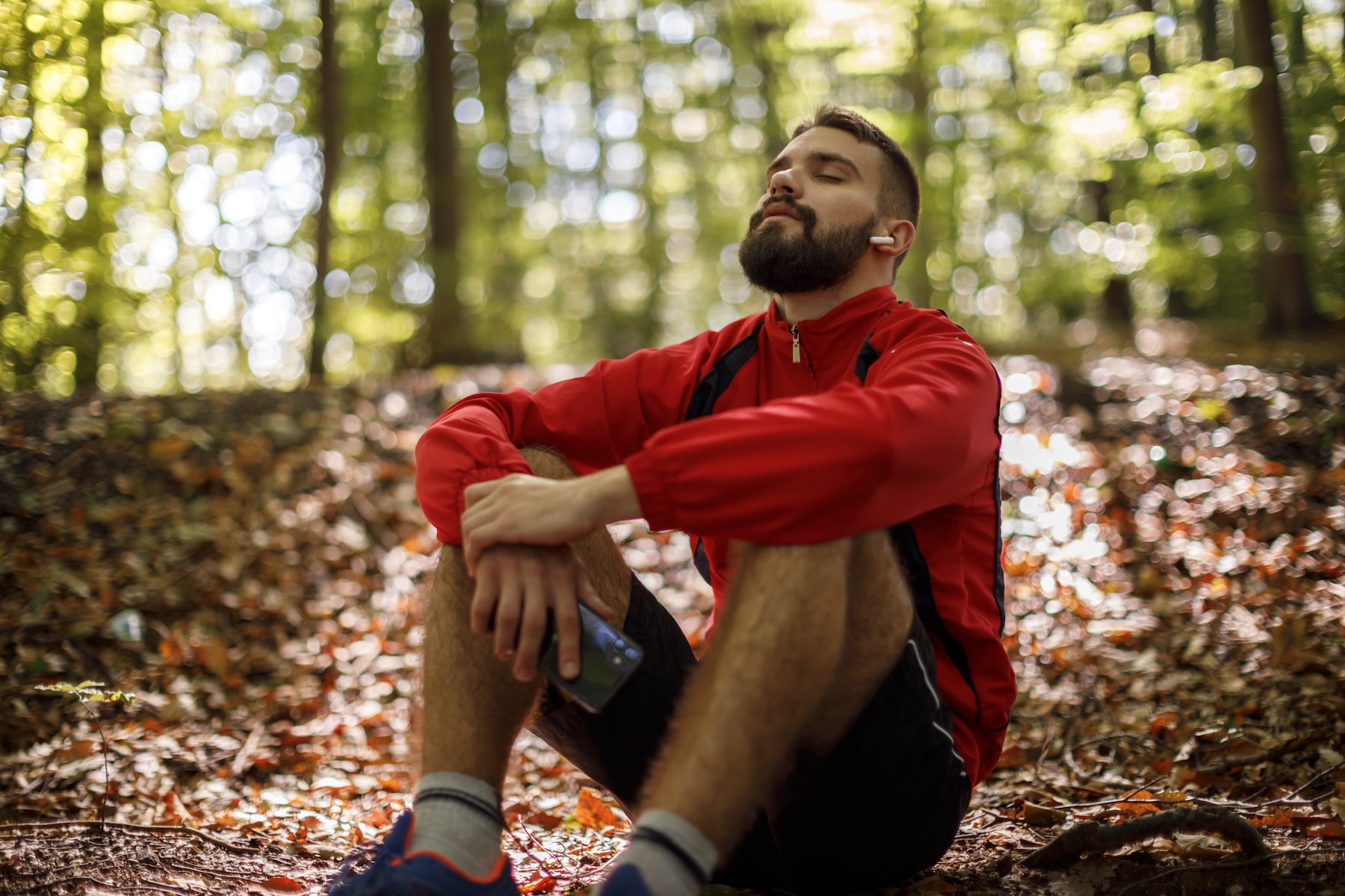 A male runner sitting down in the woods and thinking peacefully with his eyes closed. He is listening to his body.