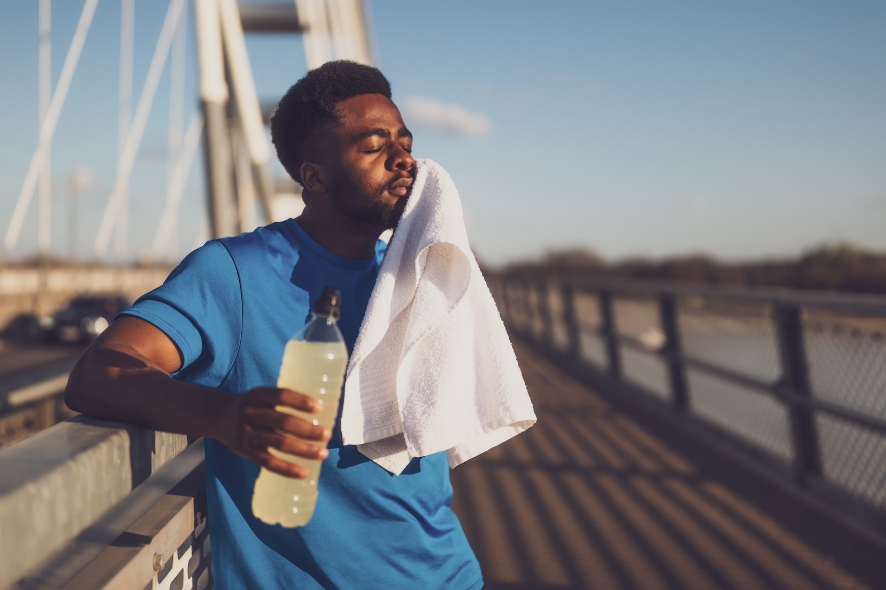 A man experiencing tooth pain after running. He is holding a white towel up to his jaw and closing his eyes while resting and holding a sports drink.
