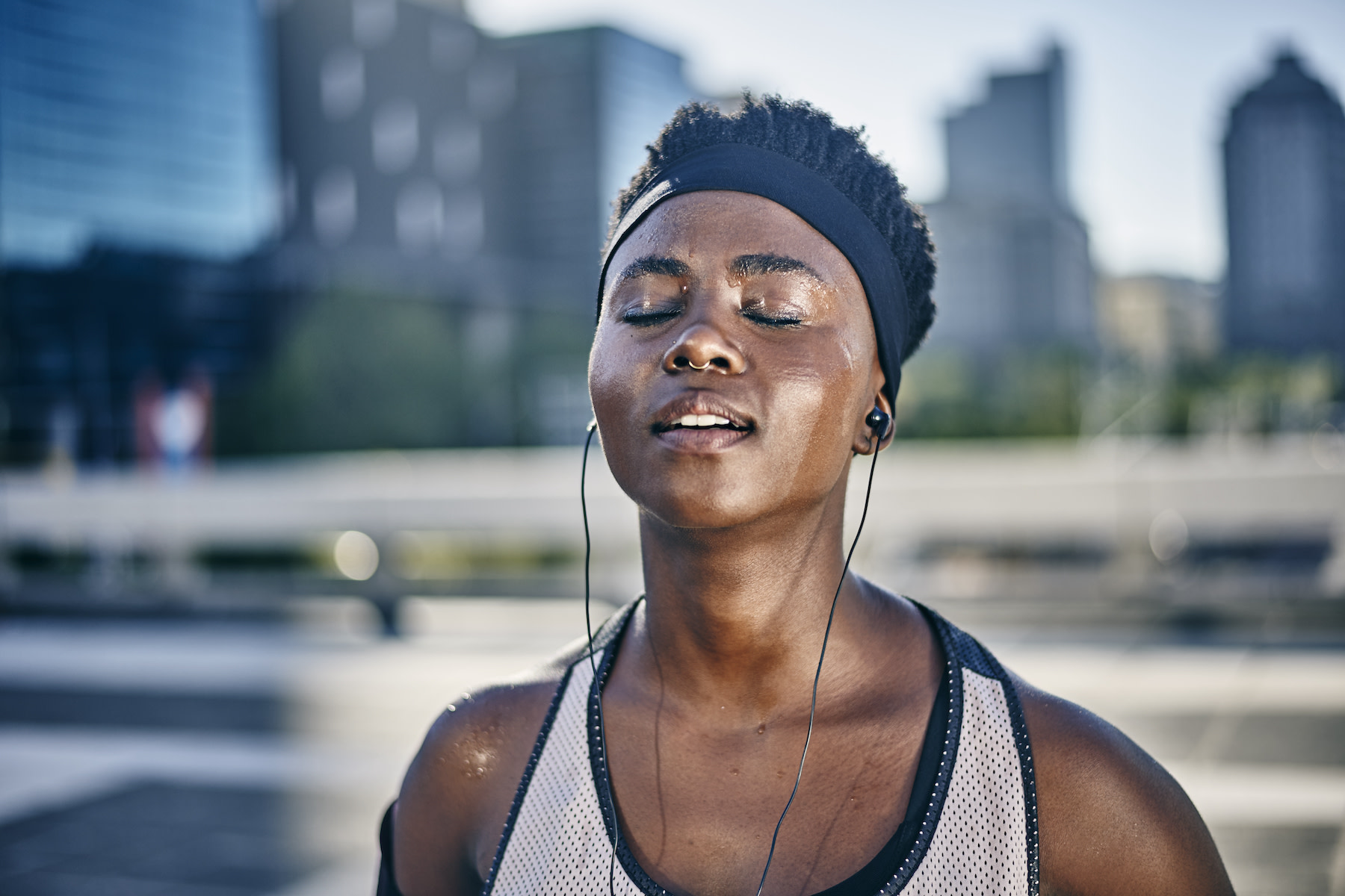 Why Do I Sweat So Much? - Image of a woman closing her eyes and standing outside sweating after a workout.