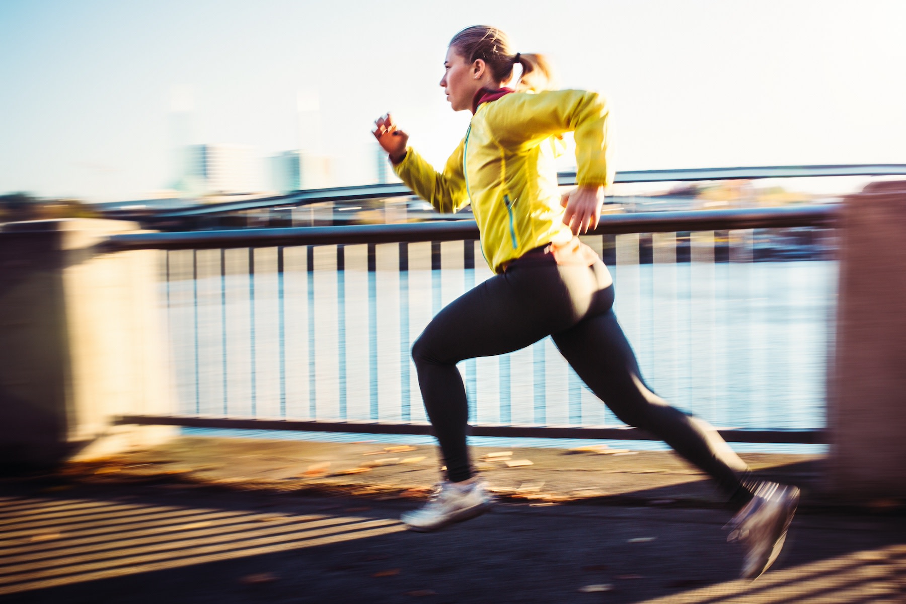 A woman practicing lactate threshold training by sprinting. She's running outside on a path near a river.