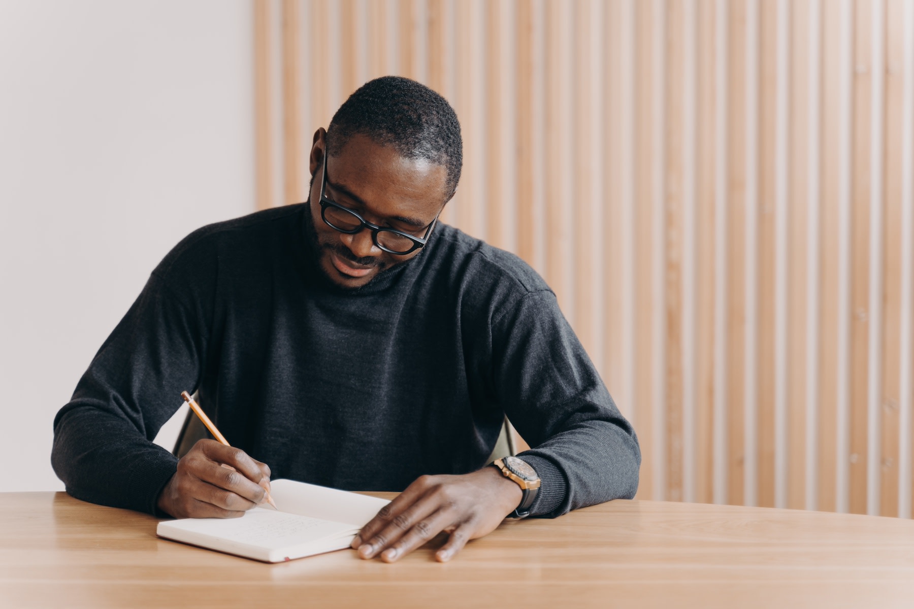 A man sitting at a desk, looking focused, and writing down manifestations.