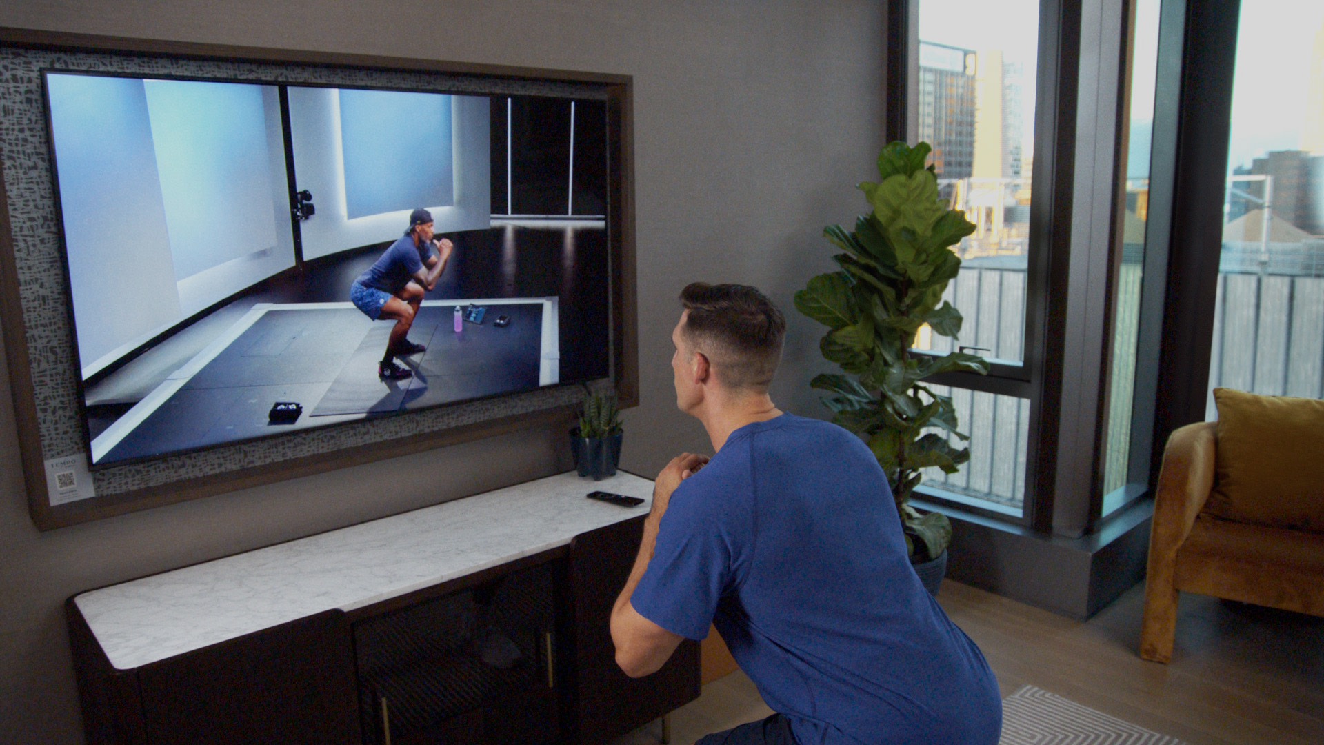 Cody Rigsby doing a Peloton bodyweight strength class with Adrian Williams on the TV in his hotel room at a Hilton hotel