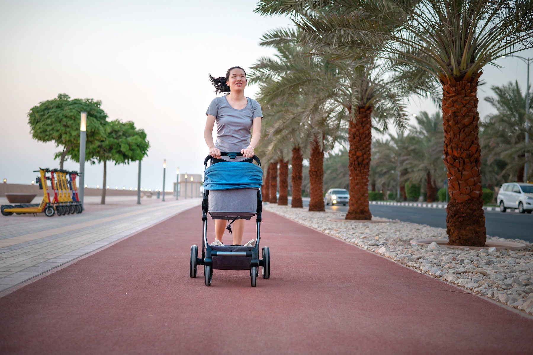 A new mom pushing her baby in a stroller while going for a postpartum workout walk outside.