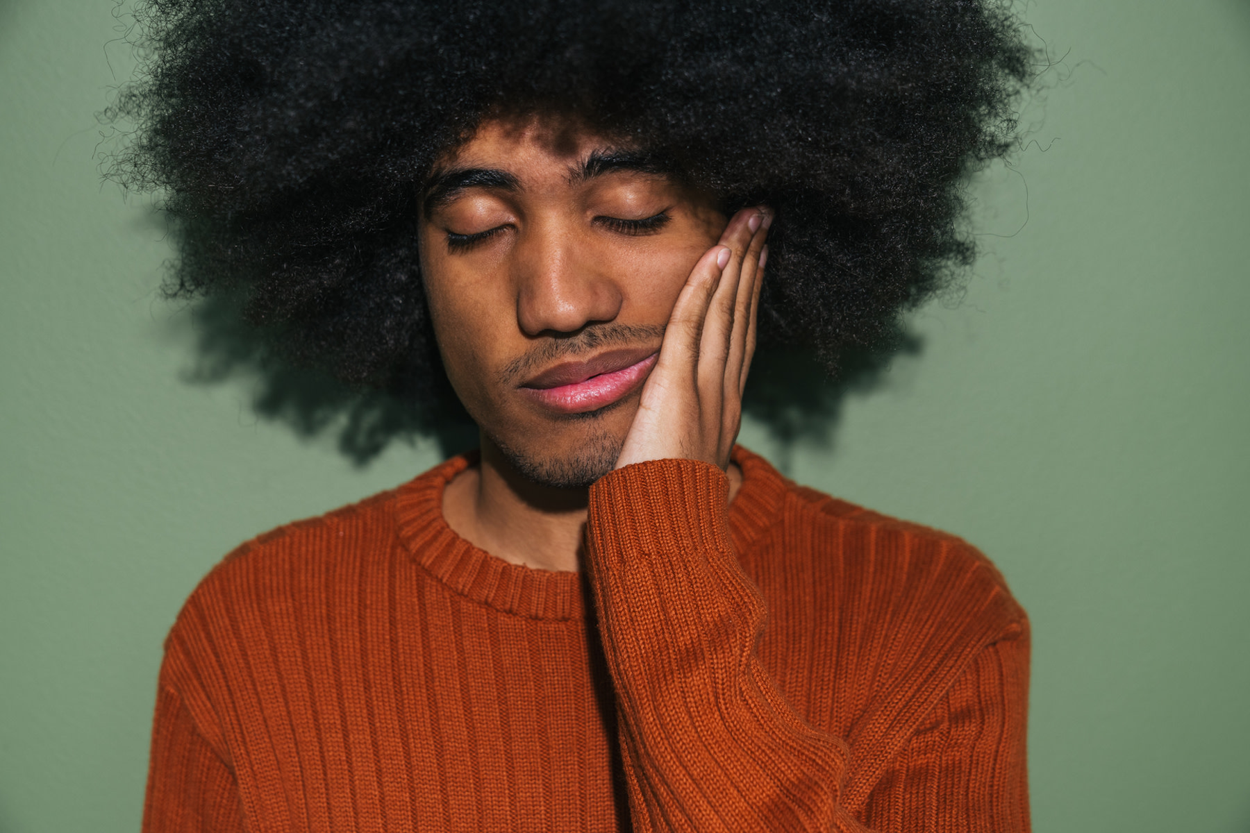 In this image for an article about feeling sleepy after eating, a man is closing his eyes and putting a hand on his cheek in tiredness.