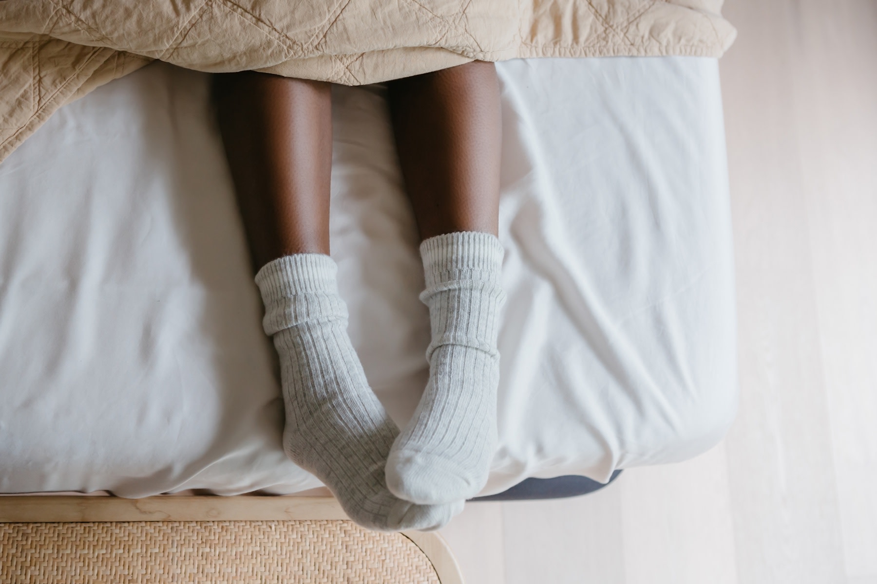 A close-up photo of a woman sleeping with socks. Her socks are gray and her feet are popping out from under the covers on her bed.